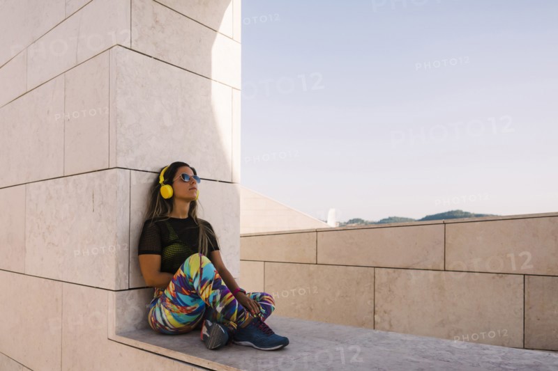 Woman wearing headphones sitting on wall