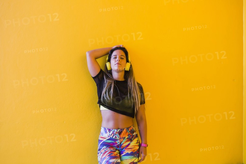 Woman wearing headphones by yellow wall