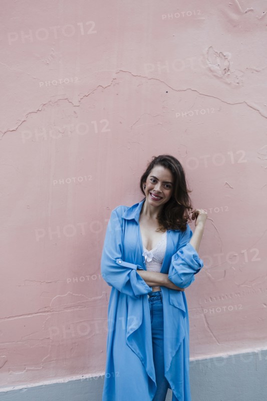 Smiling woman wearing blue by pink wall