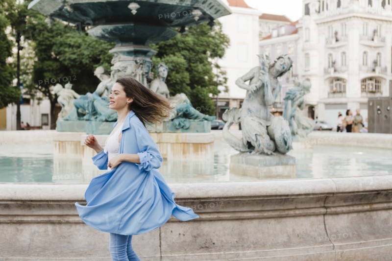 Woman wearing blue coat turning by fountain