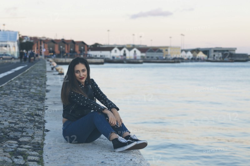 Woman sitting on footpath by sea in Lisbon, Portugal