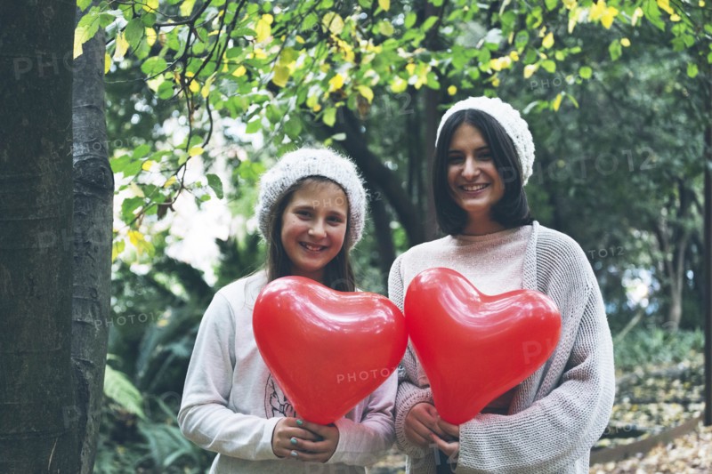 Smiling girls holding heart balloon by trees