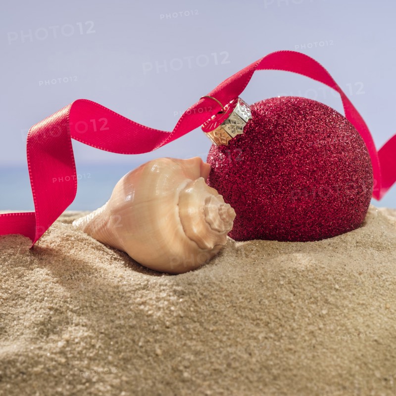 Red bauble and shell on sand