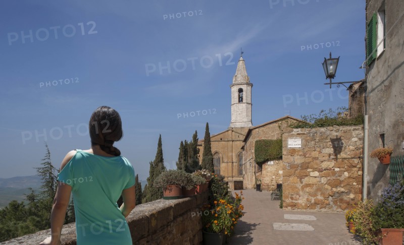 Woman by stone wall and church in Tuscany, Italy