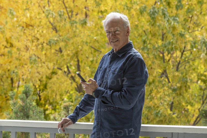 Smiling man holding phone by autumn trees