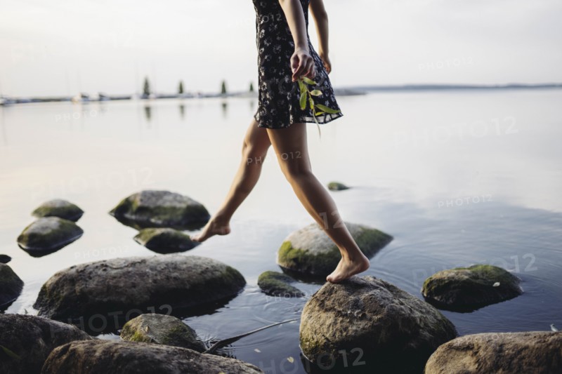 Barefoot woman stepping on rocks in sea