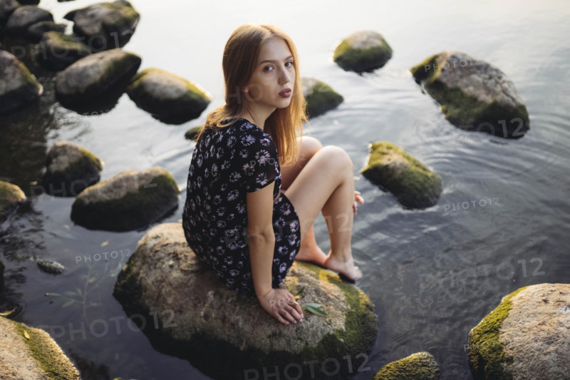 Woman wearing black dress sitting on rock in sea