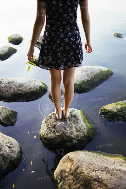 Barefoot woman standing on rock in sea