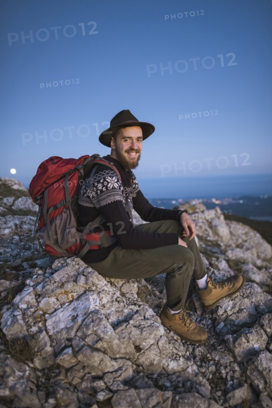 Smiling man sitting on rock at sunset