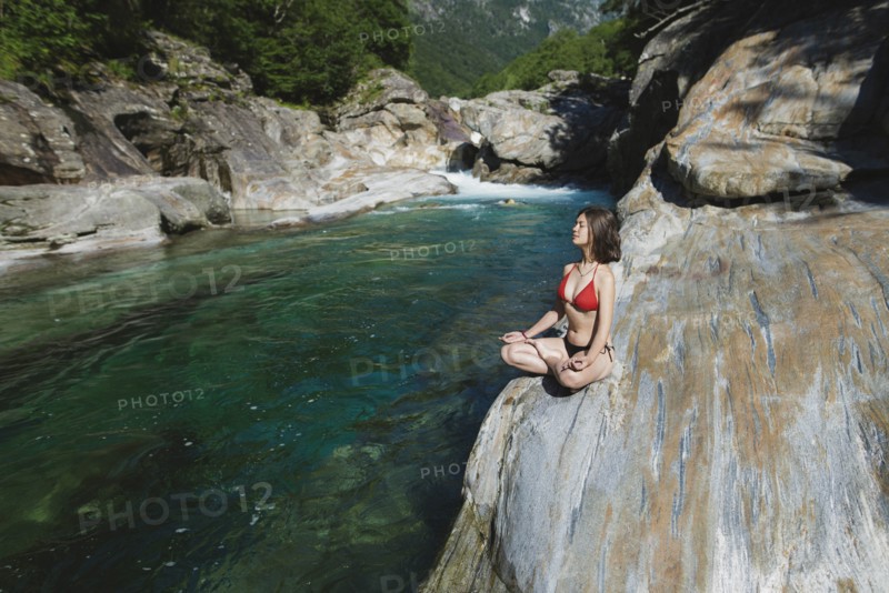 Woman wearing bikini sitting on rock by river