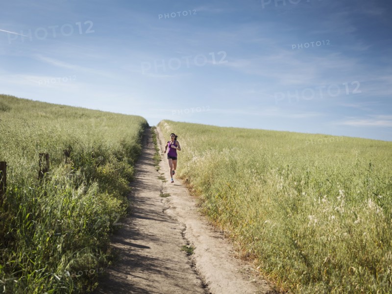 Mid adult woman jogging on path through field