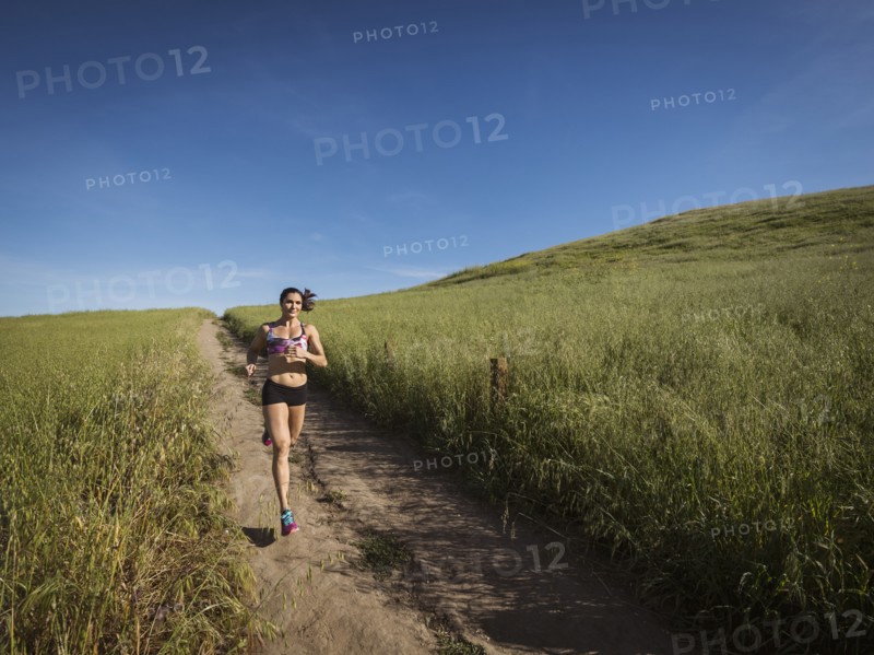Mid adult woman jogging on path through field
