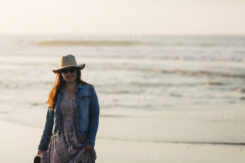 Woman in sunhat and denim jacket on beach