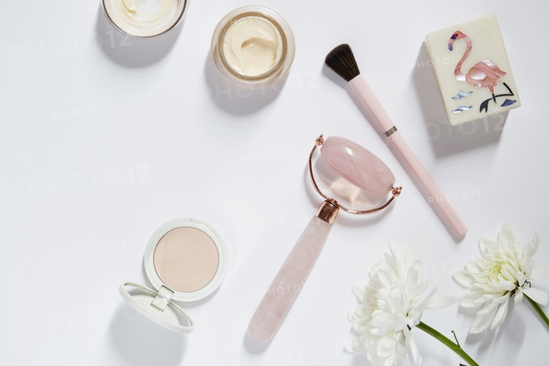 Facial roller, make-up and flowers on white table