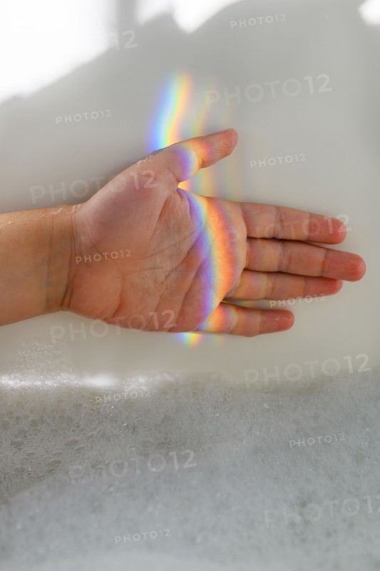 Girl's hand in rainbow light beam in bubble bath