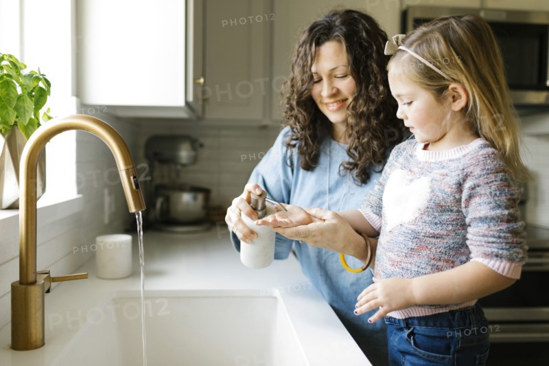 Mother and daughter washing hands in kitchen sink