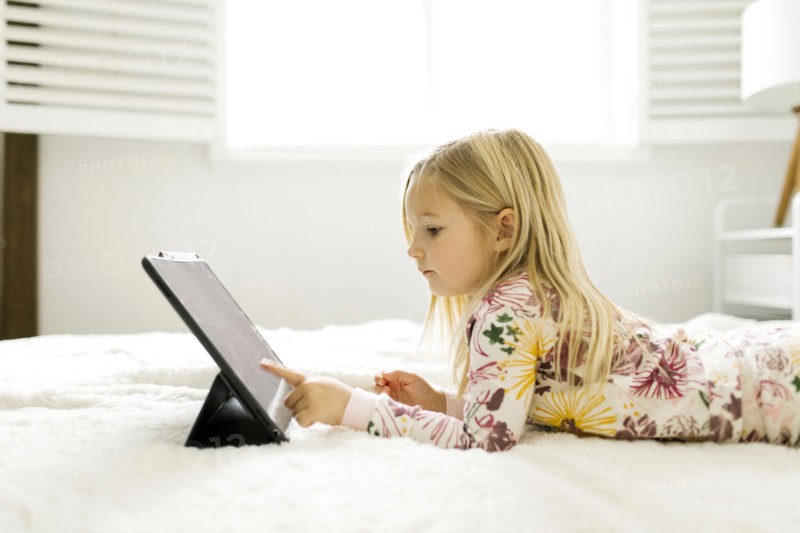 Girl in pajamas using digital tablet while lying on bed