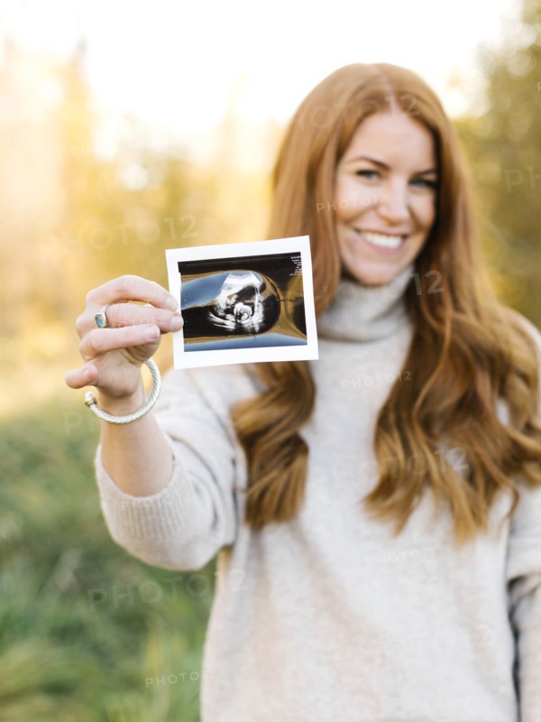 Smiling pregnant woman holding ultrasound photograph