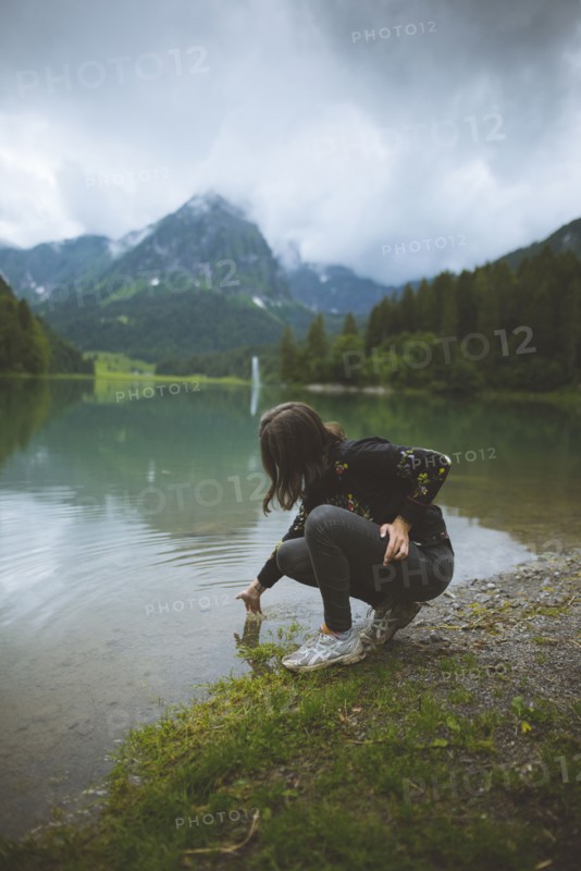 young woman crouching by lake