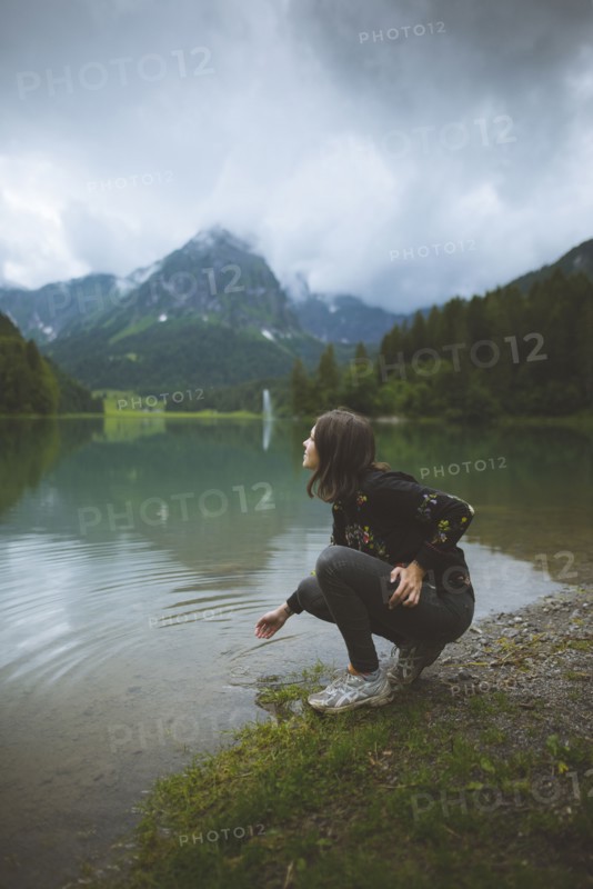 young woman crouching by lake