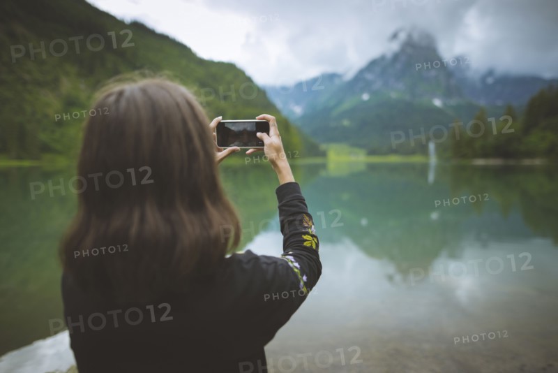 young woman photographing mountain and lake with smartphone