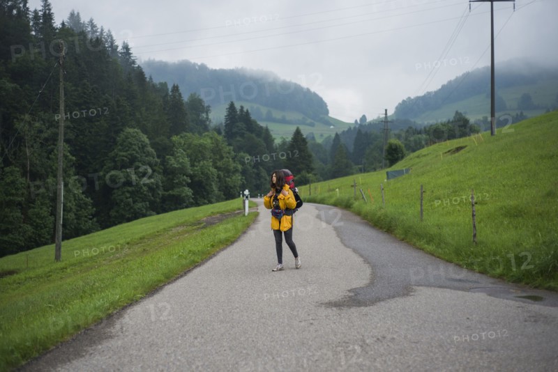 young woman with yellow jacket and backpack walking along country road
