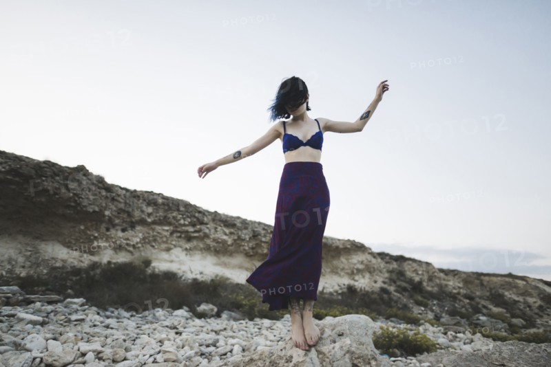 young woman in bra and skirt standing on rock
