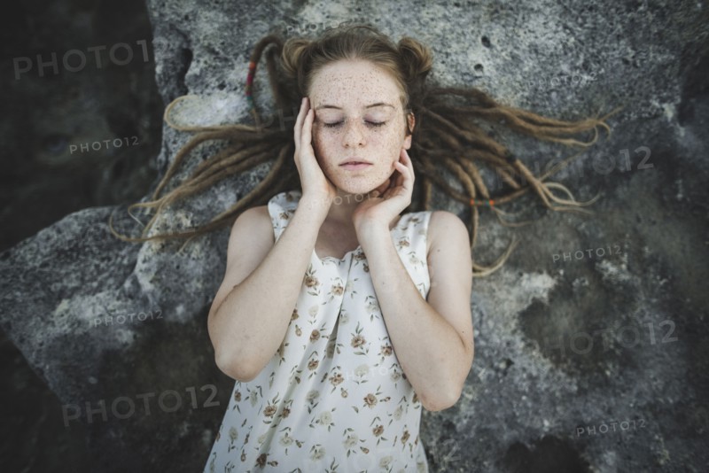 young woman with dreadlocks lying on rock