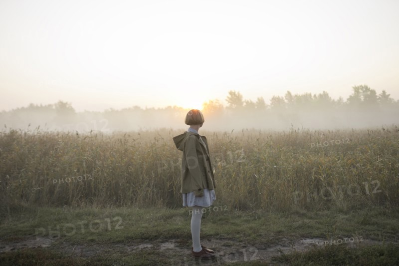 young woman by field of long grass at sunset