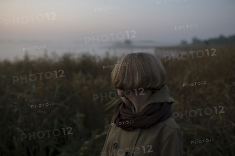 young woman in field by lake at sunset