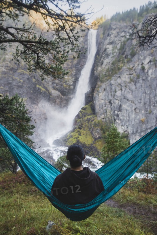 young man resting in hammock by waterfall