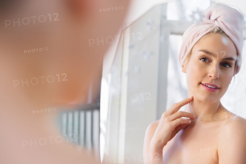 Woman wearing towel wrapped around her head looking into mirror