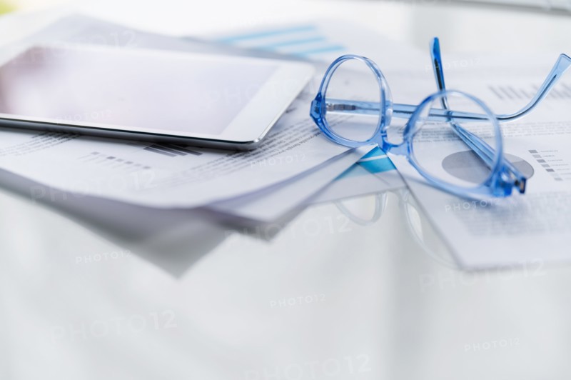 Blue eyeglasses and tablet on business papers