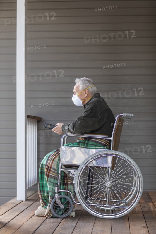 Senior man in wheelchair wearing protective mask to prevent coronavirus transmission on porch