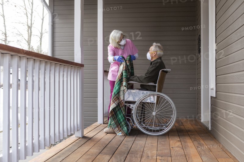 Woman and man in wheelchair wearing protective mask to prevent coronavirus transmission on porch