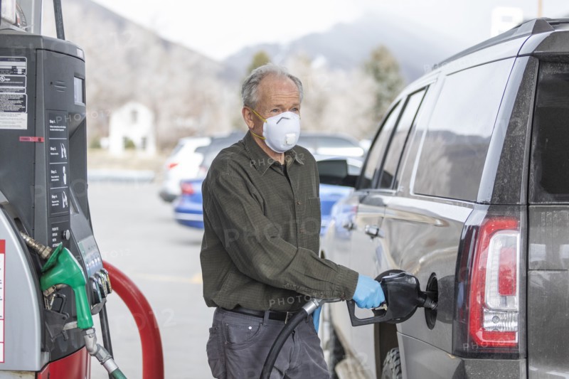 Man wearing surgical gloves and mask refueling car at gas station