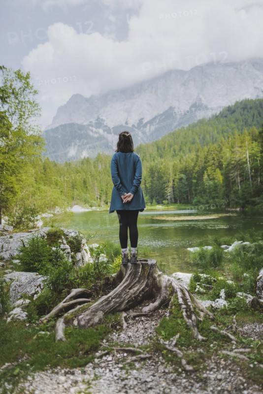 Germany, Bavaria, Eibsee, Young woman standing on stump by Frillensee lake in Bavarian Alps