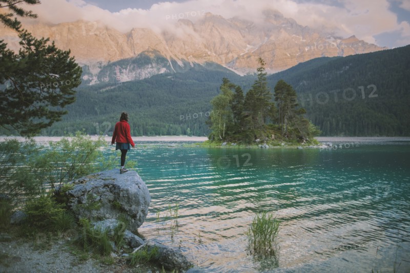 Germany, Bavaria, Eibsee, Young woman standing on rock by Eibsee lake in Bavarian Alps