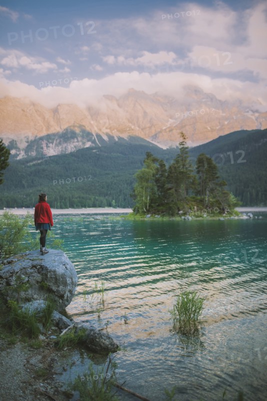 Germany, Bavaria, Eibsee, Young woman standing on rock by Eibsee lake in Bavarian Alps