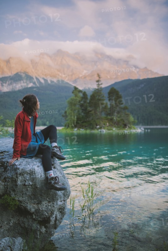 Germany, Bavaria, Eibsee, Young woman sitting on rock and looking at scenic view by Eibsee lake in Bavarian Alps