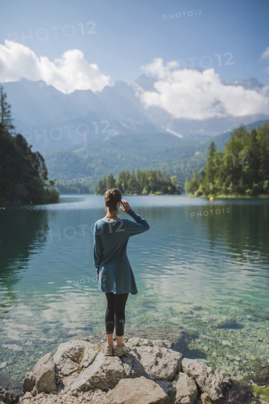 Germany, Bavaria, Eibsee, Young woman standing on rock at shore of Eibsee lake in Bavarian Alps