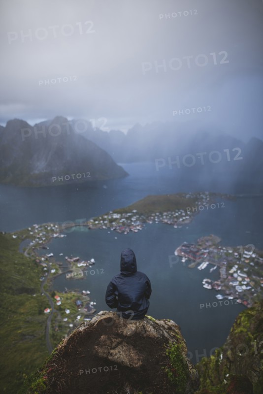Norway, Lofoten Islands, Reine, Man looking at fjord from Reinebringen mountain during rain