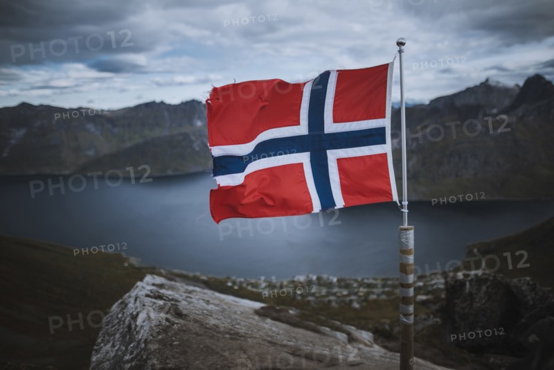 Norway, Senja, Norwegian flag with fjord and mountains in background