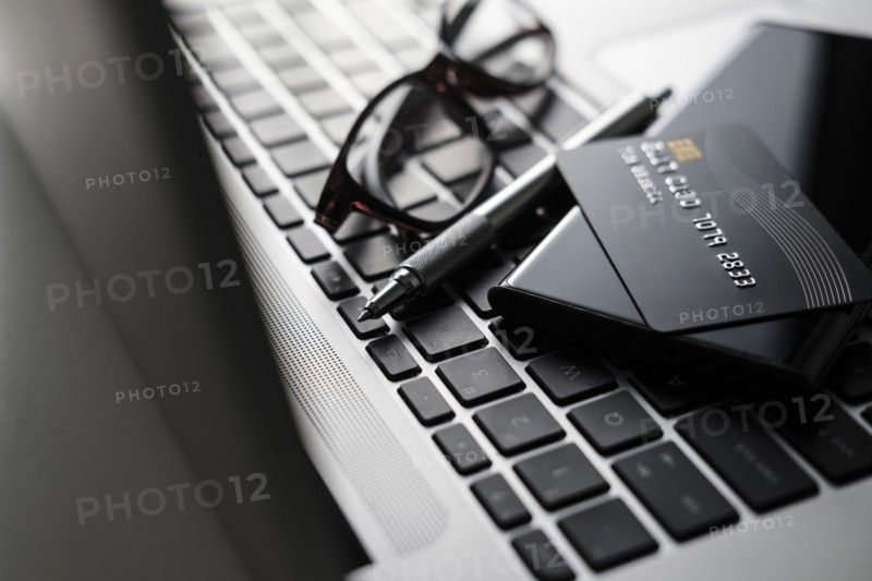 Credit card, smart phone, pen and glasses on laptop keyboard