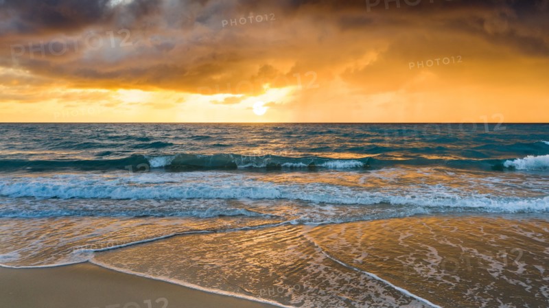 Beach under dramatic sky at sunset