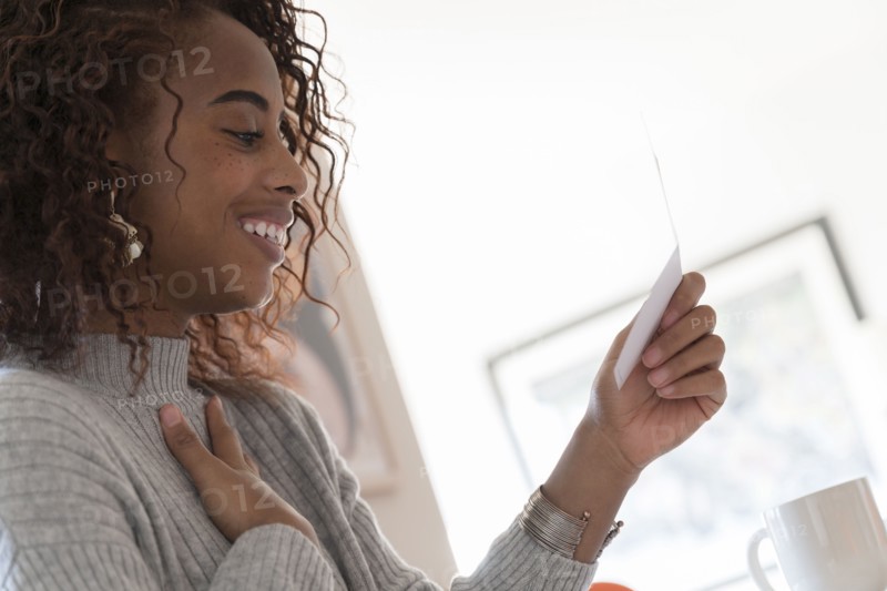 Smiling woman reading card touching her chest