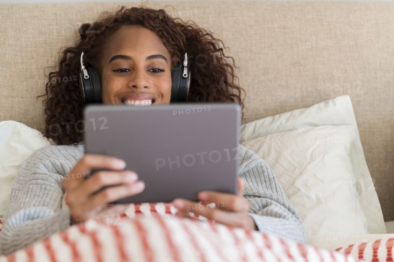 Smiling woman using tablet with headphones in bed