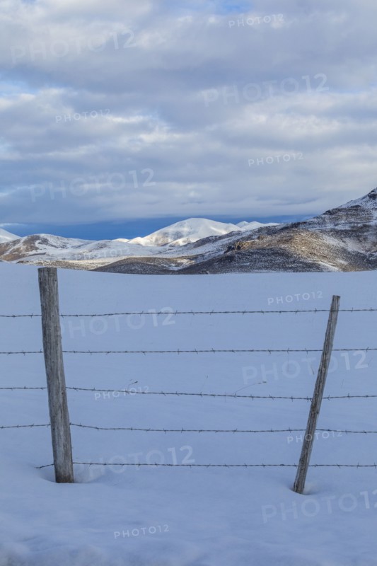 Barbed wire fence in snow with mountains in distance