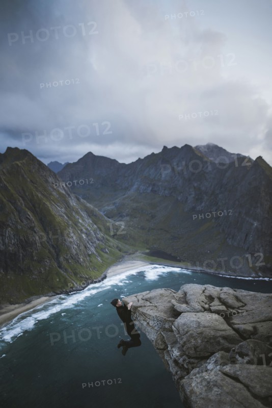 Man hanging on cliff at Ryten mountain in Lofoten Islands, Norway