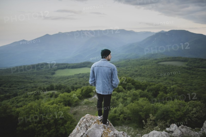Man standing on cliff by mountain and forest